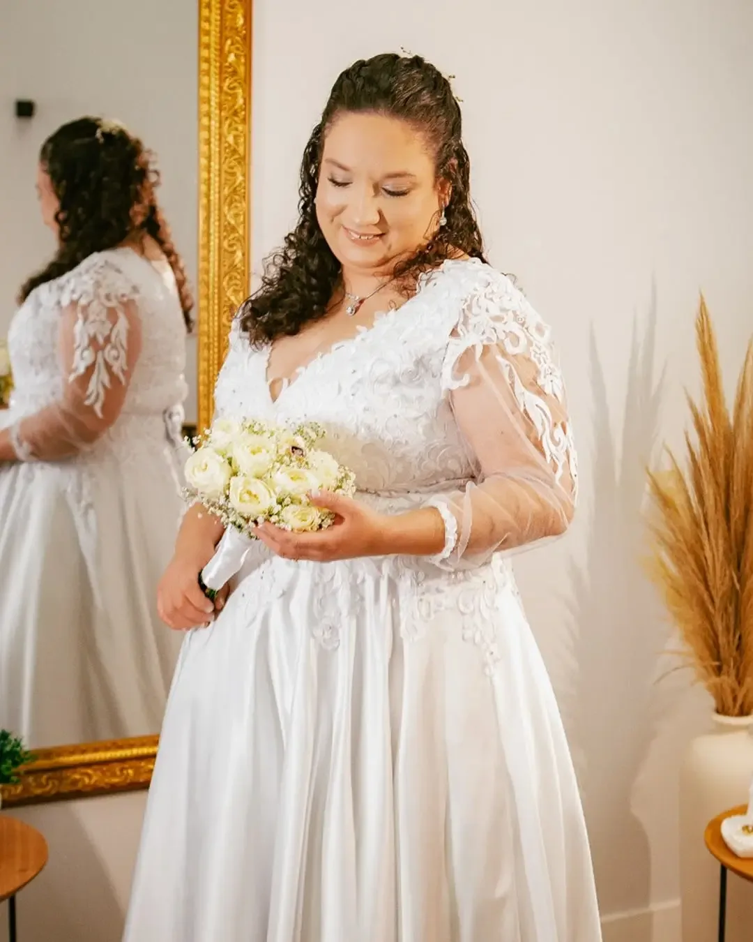 Noiva com vestido de renda e buquê durante os preparativos.