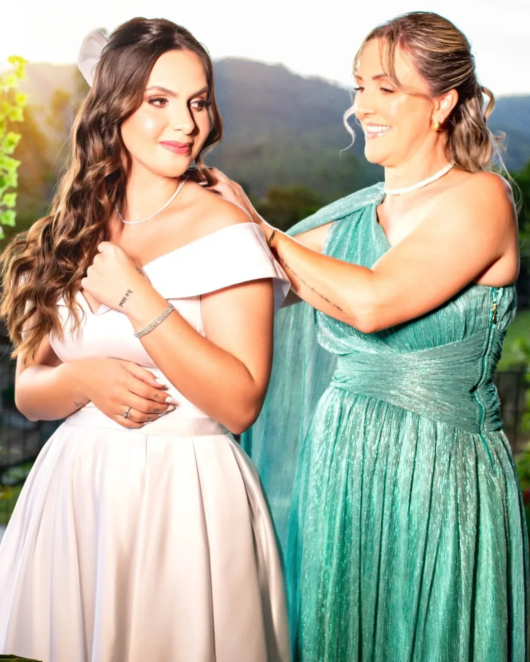 Mulher de vestido verde ajudando a noiva com o vestido.