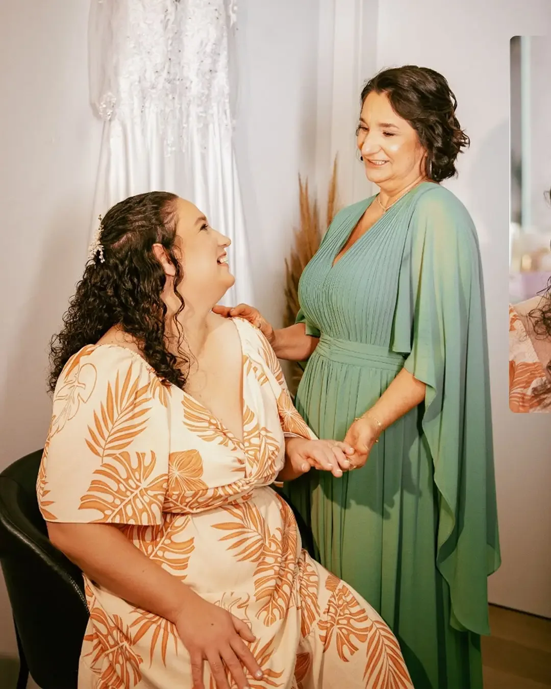 Noiva e mulher de vestido verde sorrindo em um quarto.