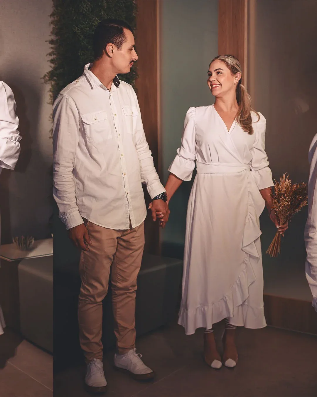 Casal com roupas claras diante de uma porta durante o casamento civil.