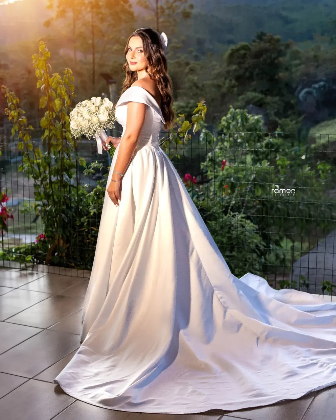 Noiva com vestido branco e buquê ao ar livre no fim da tarde.